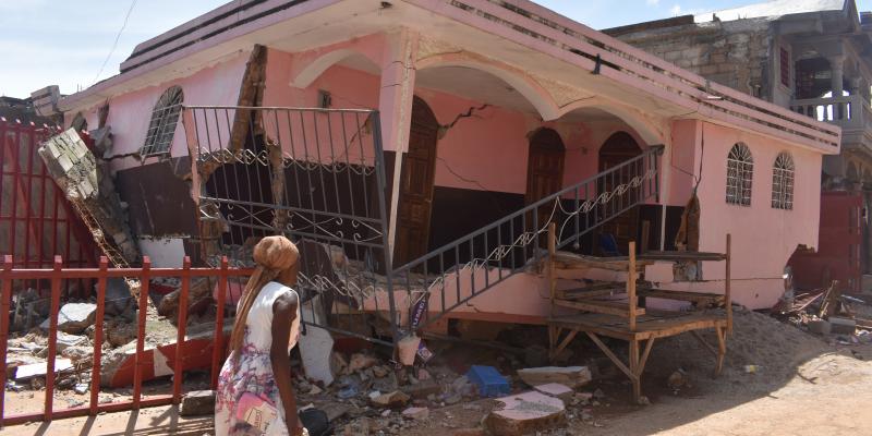 A woman walks by a partially collapsed house in Haiti.