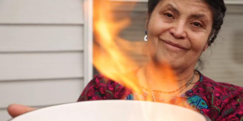 Maria holding up a bowl that contains a fire burning her mortgage papers.