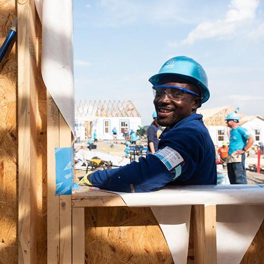 Bizimana smiling at the camera as he works on a built site in a blue Habitat hardhat.