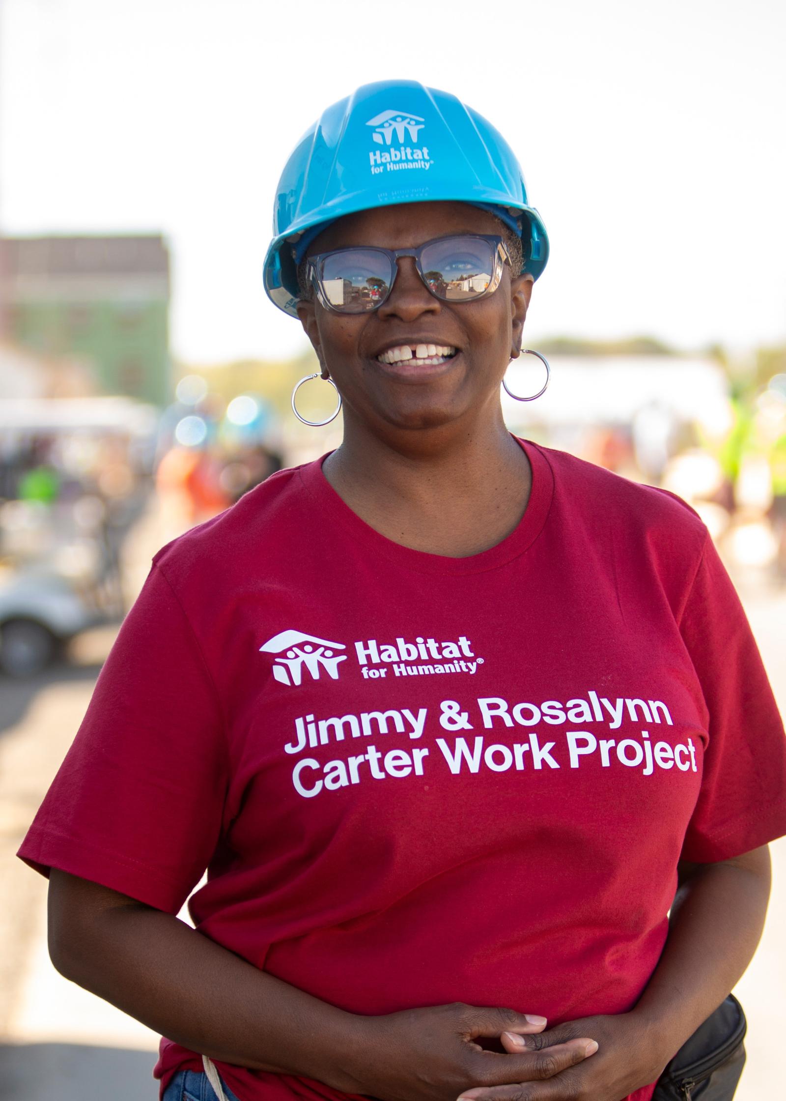 Bridgette in a blue hardhat smiles at the camera on the buildsite.