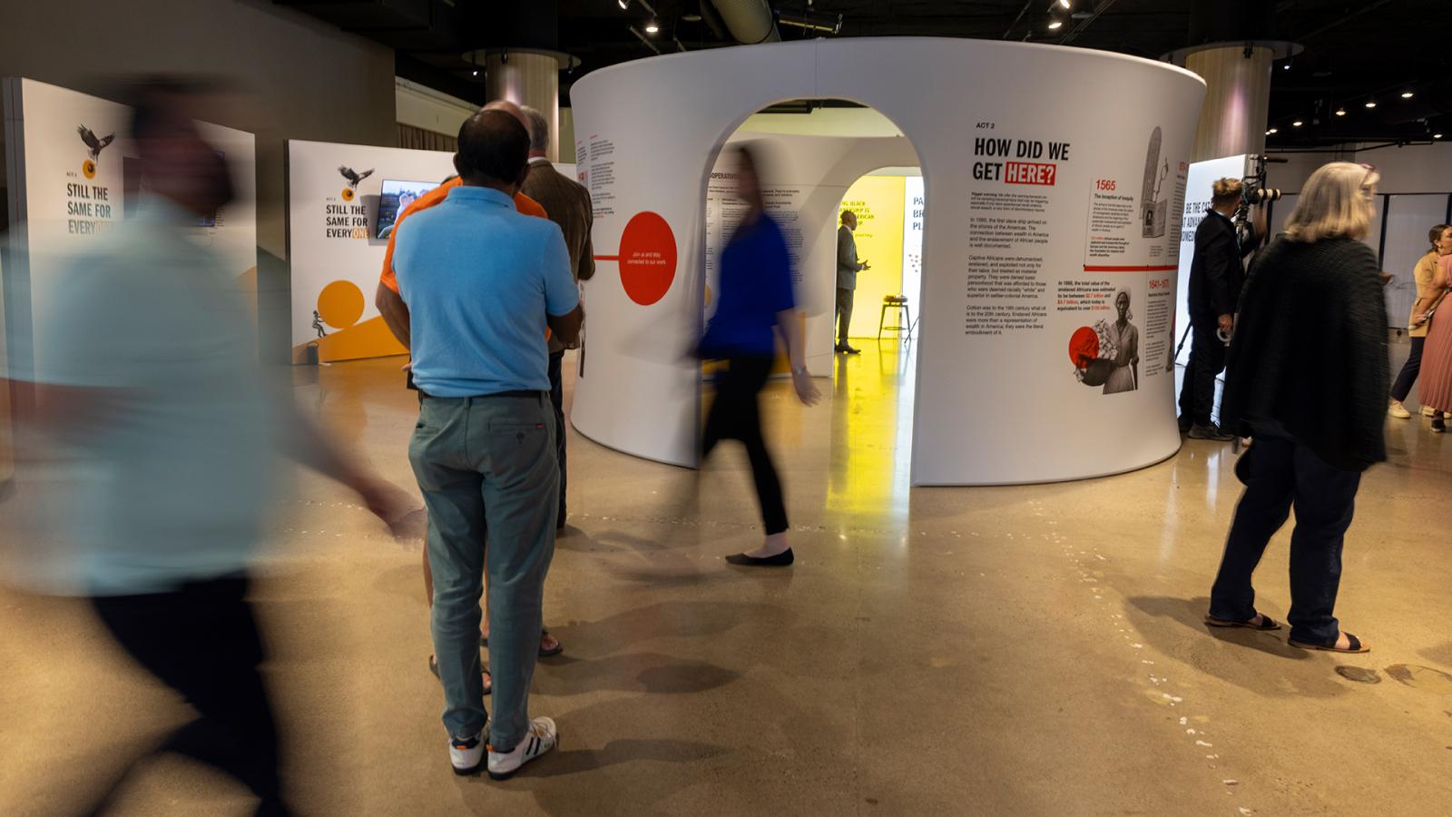 Visitors exploring the Advancing Black Homeownership exhibit. The figures are blurred to indicate movement and action.