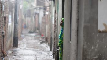 Woman in green sari staring to the left from a door frame into an alleyway. 