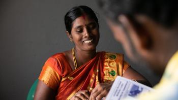 A woman in a colorful sari smiles as she sits at a table with a colleague.