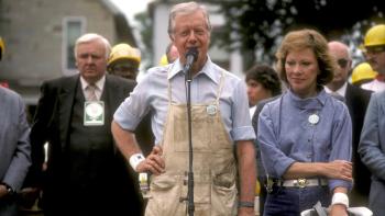 President and Mrs. Carter stand in front of a microphone at a Carter Work Project build.