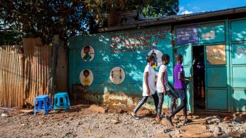 Three children walking into a building painted bright blue. 