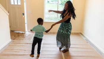 A mother and her young son dancing in an empty living room in their new Habitat home.