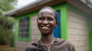 A woman is smiling outside her home in Kenya.