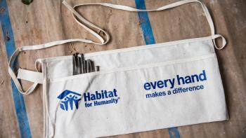 Habitat for Humanity tan workers apron with blue logo. Nails in the left pocket on top of butcher paper and painters tape.