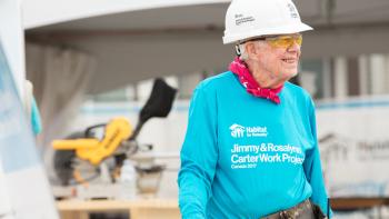 President Carter smiling on Habitat build site wearing hard hat, red bandana, and bright blue Habitat shirt