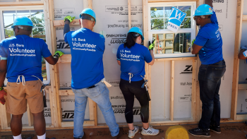 U.S. Bank volunteers raising a wall frame together on a build site