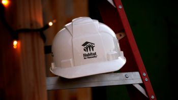 A ladder with white string lights wrapped around it and a white hardhat with Habitat logo sitting on one of the steps. 