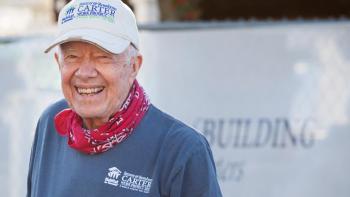 President Carter smiling wearing a red bandana, a white Habitat hat and a blue Habitat shirt.