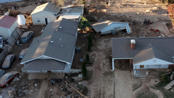 Overhead shot of a muddy landscape with significant hurricane damage to multiple houses and several ruined cars.