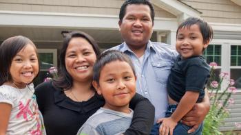 Familia de cinco personas sonriendo frente a la casa.