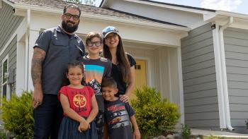 Family of four smiling in front of their Habitat home