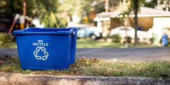 blue recycling bin on curb with cars in the background.