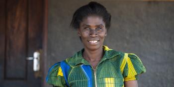 Habitat homeowner Joyce smiling in front of her home in bright green dress.