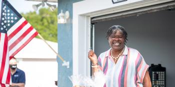 Lisa holding her key in front of her new home with an American flag hanging on the house.