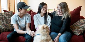 Candance and her two kids sit on their couch with their Golden Retriever dog on their floor.