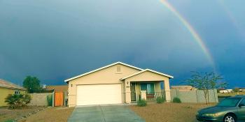 House with rainbow in the background against a dark sky.