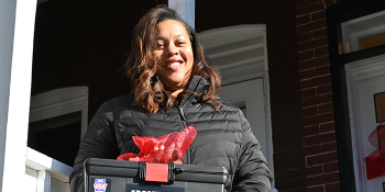 Woman smiling holding a box with a bow on it in front of her Habitat home.