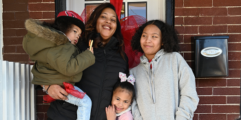 Mom and three kids smiling in front of home.