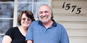 Smiling man and woman in front of a house.