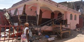 A woman walking past a partially collapsed home.