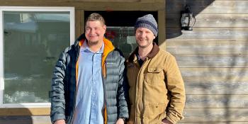 Two men stand in front of a house