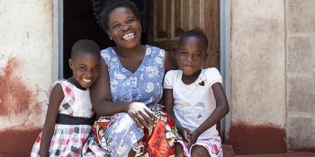 Photo: a women and two children from Zambia sitting on stairs in front of their house