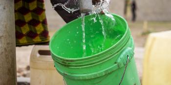 A woman fills up a green bucket with water from a water kiosk.