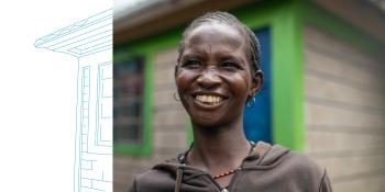 A young woman smiles as she stands in front of her Habitat home, a concrete brick house with bright green trim and a blue door. The shape of the house extends into a lineart illustration.