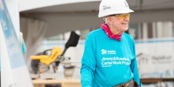 President Carter smiling on Habitat build site wearing hard hat, red bandana, and bright blue Habitat shirt