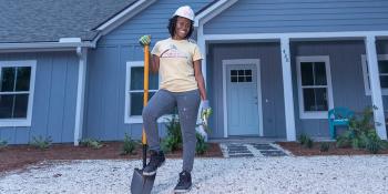 Woman smiling while wearing a hardhat and holding shovel in front of new Habitat house.