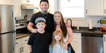 Young couple pose smiling with their elementary-aged son and daughter in the tidy kitchen of their Habitat home.