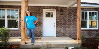 Woman in blue shirt standing on front stoop of her Habitat home.