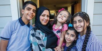 Mother with four children smiling together in their doorway.