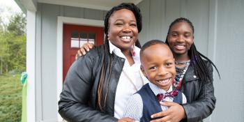 Mother with daughter and young son smiling in their doorway.