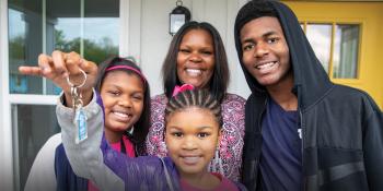 Mother smiling with three children and youngest child is holding up a house key.