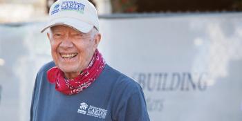 President Carter smiling wearing a Habitat-branded shirt and ball cap and a red bandana