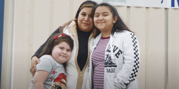 Dina smiling and embracing her two daughters.