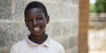 young Zambian boy smiling in front of concrete block Habitat home.