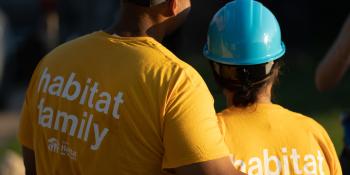 A pair of homeowners in yellow shirts that read, "habitat family," hugging during sunrise.