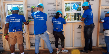 U.S. Bank volunteers raising a wall frame together on a build site