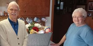Smiling elderly couple standing in their kitchen with large gift basket