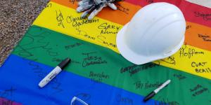 Photo of a signed rainbow flag with a hardhat on top.