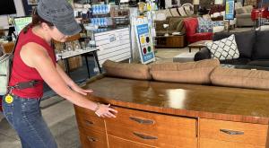 Woman in a red tank top, jeans and a gray hat inspecting a dresser.