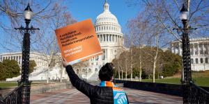 A woman holding an orange Habitat advocacy sign stands with her back to the camera as she looks toward the Capitol building in Washington D.C.