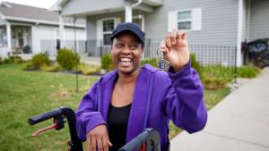 Aretha  holding up a key, smiling in her driveway.