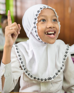 Young Indonesian student wearing a head covering in a school setting with an excited engaged expression